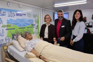 Jasmin Modis und Thorsten Hitzel (Martin Luther Stiftung Hanau) sowie Salomé Eggler (Google) im Mobilen Skills Lab (v.l.n.r.). Im Vordergrund ist die Pflege-Simulationspuppe zu sehen. (Foto: Martin Luther Stiftung Hanau)